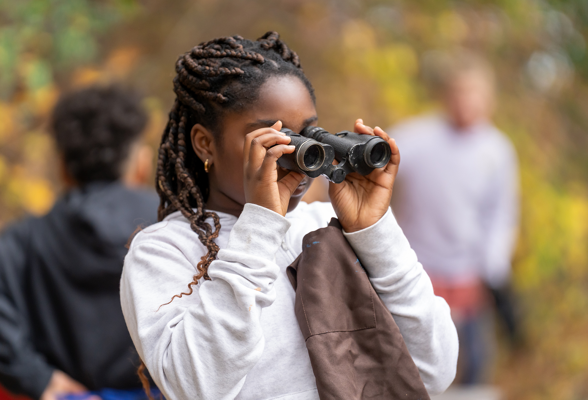 Student looking through binoculars outside on a fall day.