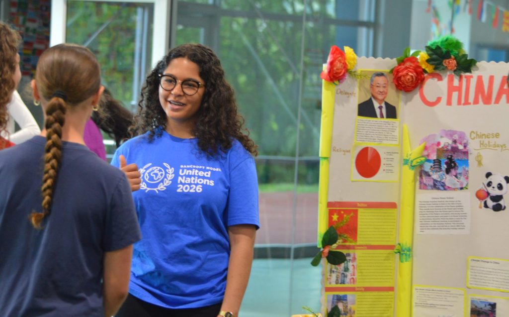 A Bancroft School Middle School student dressed in a Model UN t-shirt explains what she learned to a group of peers.