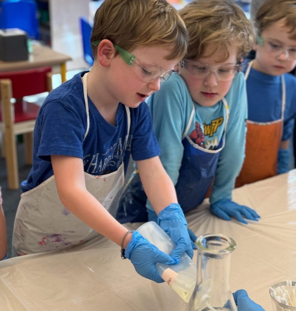 Lower school students wearing aprons and goggles in a lower school science class.