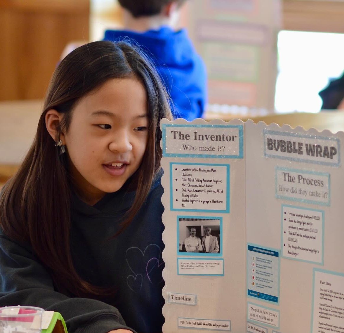 Lower School student sitting at table describing her tri-fold display.