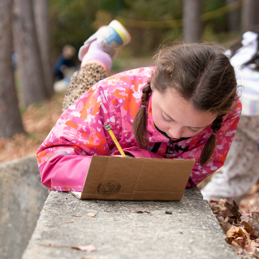 Student is outside writing in a science journal at Bancroft School in Worcester, MA.