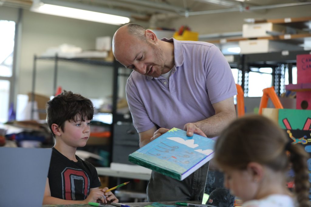 Art studio with teacher speaking with younger student.