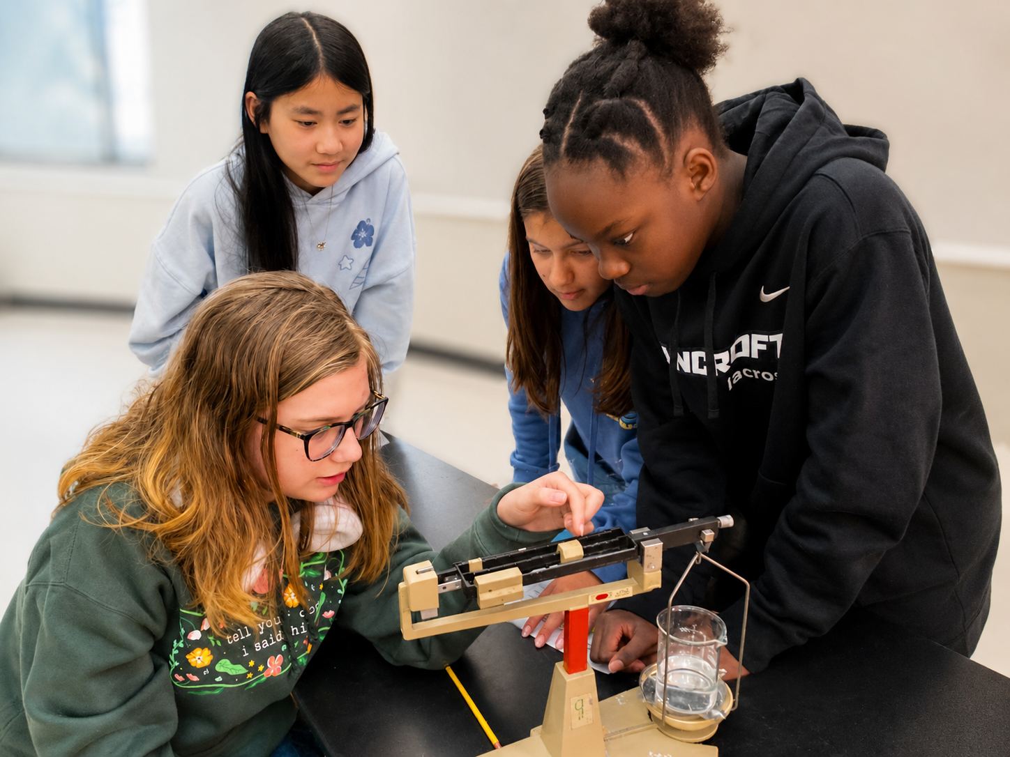 4 students look at a scale in science class/